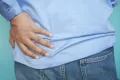 a person wearing jeans and blue shirt holding his lower back for uti blood in urine