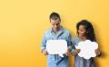 A man and a woman stand side by side against a yellow background, each holding a blank speech bubble cutout. The man is looking down at the rectangular speech bubble, while the woman looks at him and holds a cloud-shaped speech bubble.