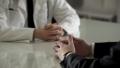 Two individuals sit across from each other at a table, one in a white coat and the other in a dark jacket. The focus is on their hands resting on the table, suggesting a serious conversation. The background is blurred, emphasizing the interaction between them.