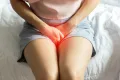 a woman sitting on a bed in pain with her hands on her pelvic area