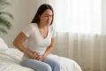 Woman sitting on bed with abdominal pain, highlighting symptoms related to UTI discharge in women.