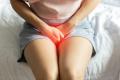 A woman sitting on a bed in pain, hands on her pelvic area due to a urinary tract infection.
