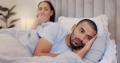 Man in his bed sad about his premature ejaculation, in the background is his wife