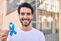 Man in a white shirt holding a blue ribbon against prostate cancer